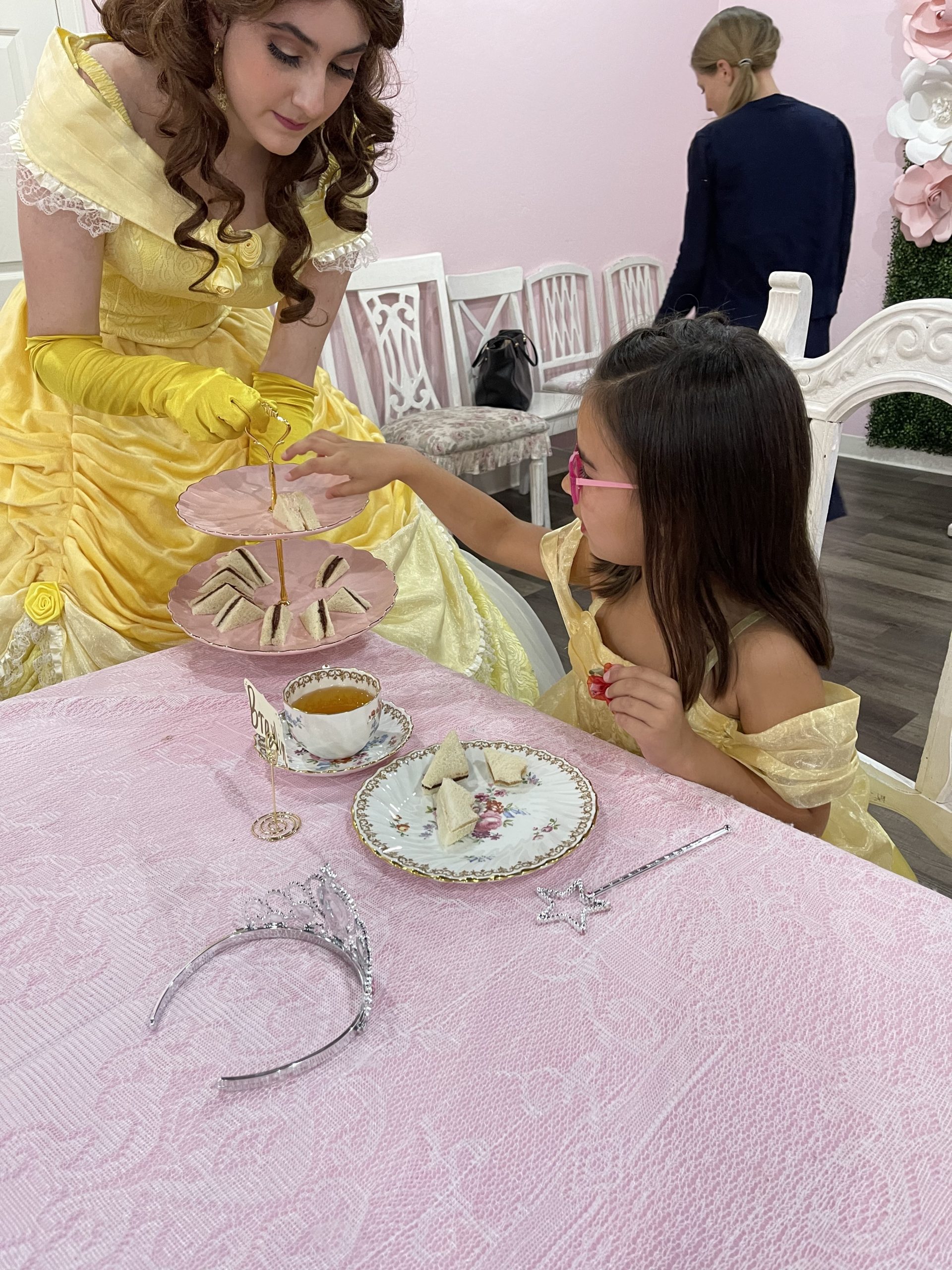 Belle serving tea sandwiches to a little girl dressed as Belle at a birthday party.