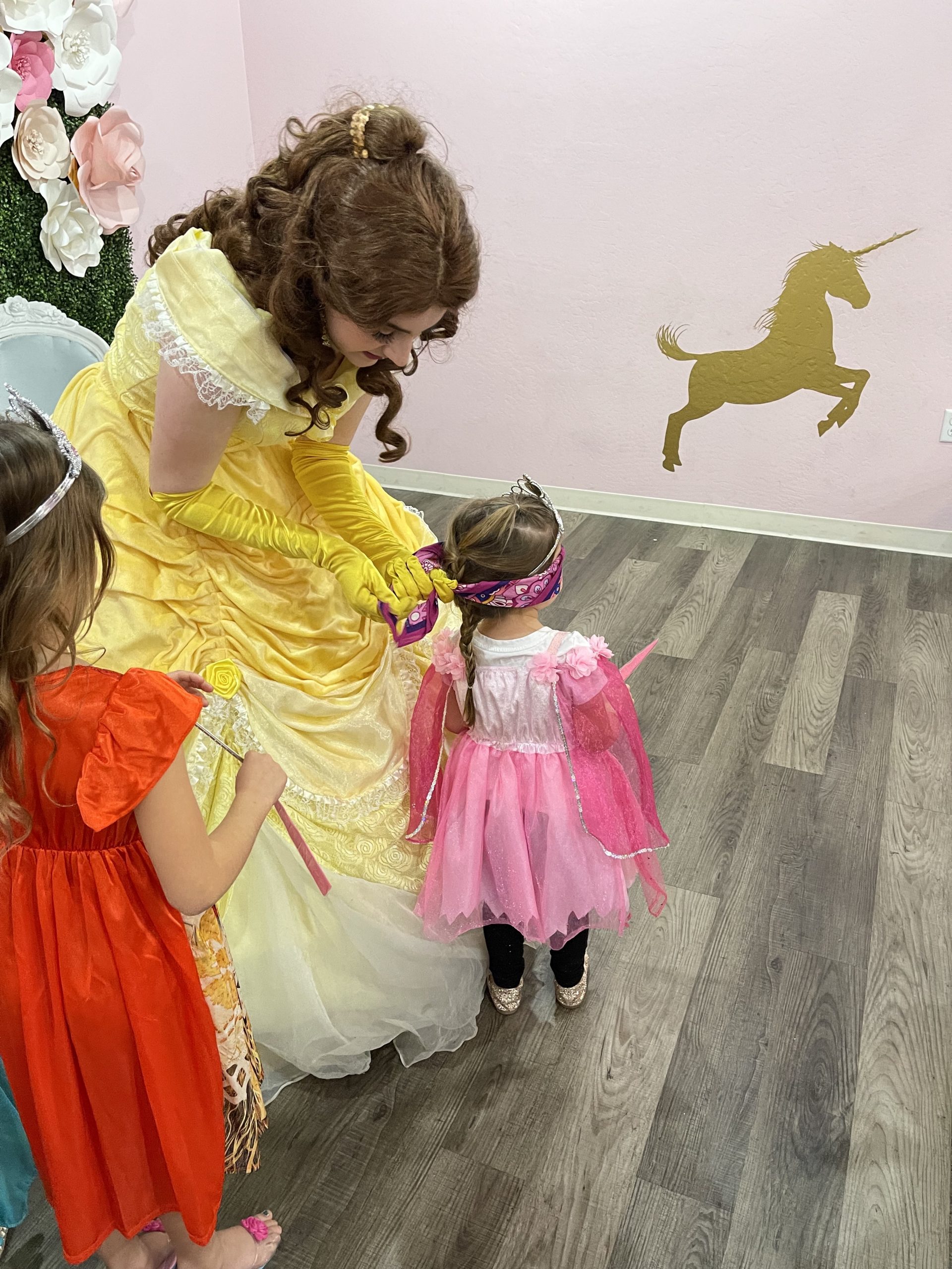 Belle helping a little girl play Pin the Horn on the Unicorn
