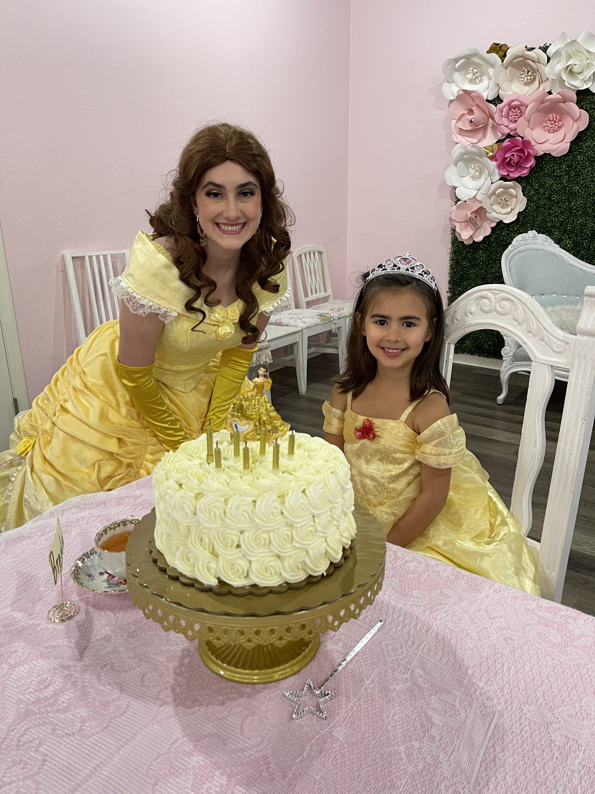 Belle posing next to a little girl dressed as Belle with a Belle-themed birthday cake.