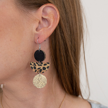 Woman's ear showcasing a dangly earring with a small black circle on top of a leopard print half circle on top of a glittery gold circle.