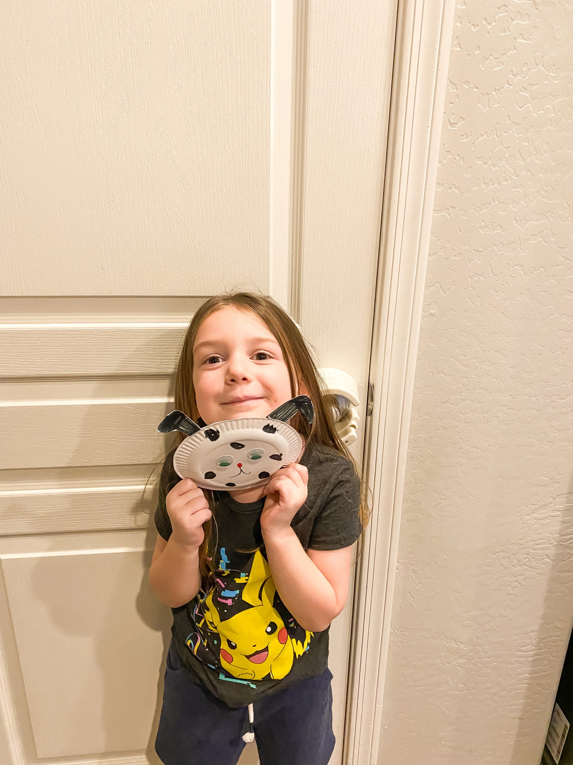 4 year old girl holding up a homemade craft of a Dalmatian made out of a paper plate