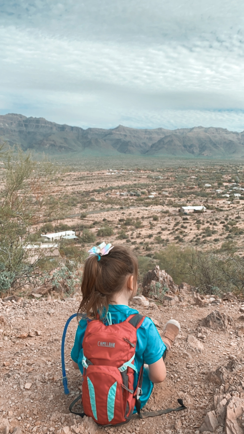 Little girl sitting on a desert hill overlooking nearby mountains.